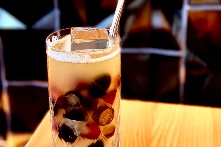 A peach-colored Fortified Mule in a clear Collins glass with halved grapes, a clear cube, and a metal straw
