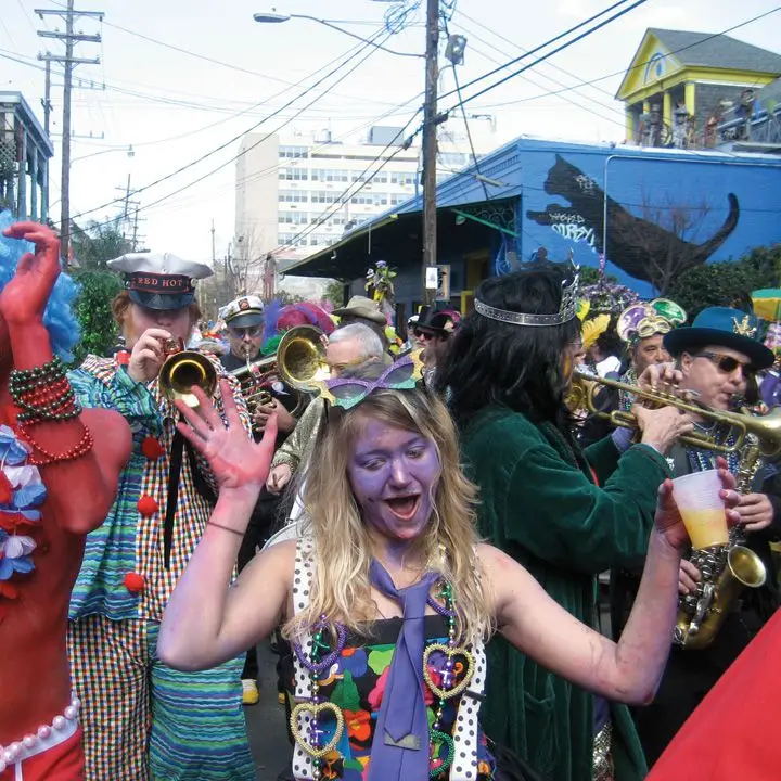 mardi Gras revelers with a woman in the cetner in purple face point and a trumper player behind her