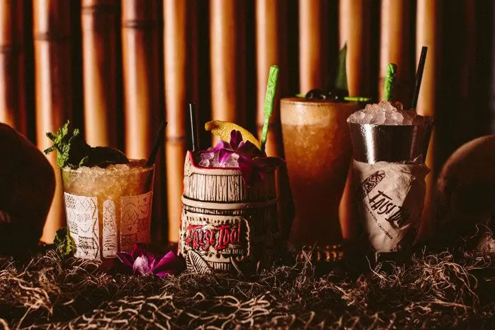 A row of four tiki drinks in various glass and ceramic vessels