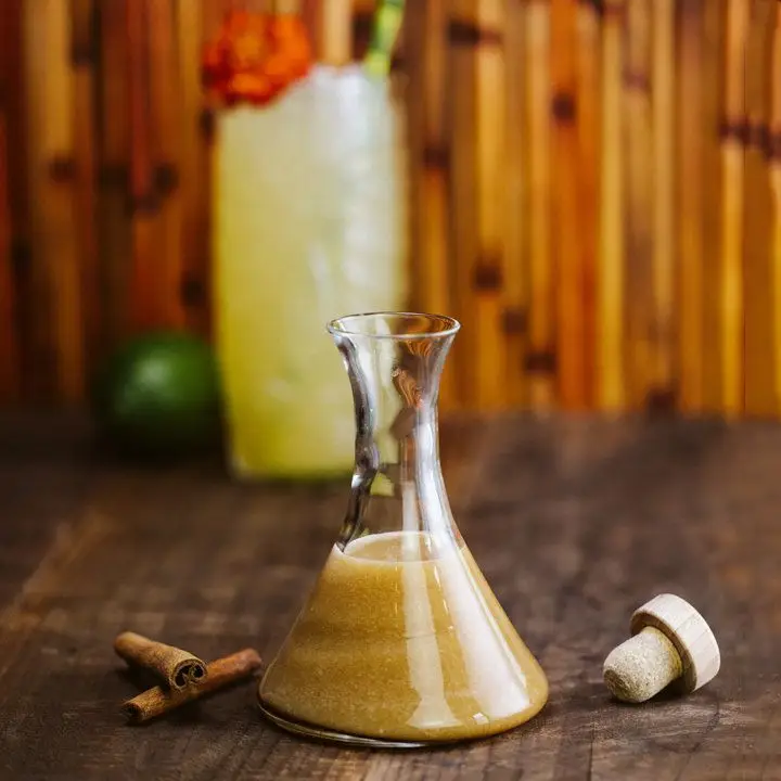 A beaker of golden, almost sparkly gardenia mix on a wood surface with a bamboo background