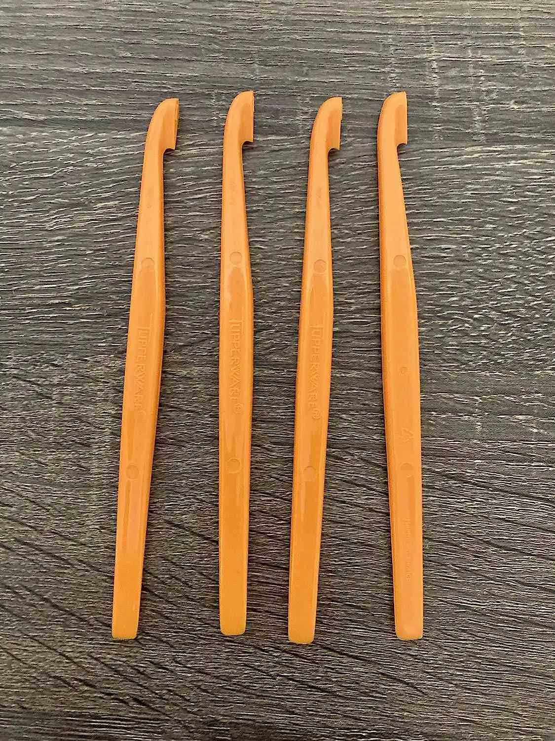 Four orange Tupperware citrus peelers on a wood background
