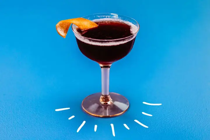 Photo illustration of deep red Improved Dunlop cocktail in coupe glass on blue background with white hand-drawn lines