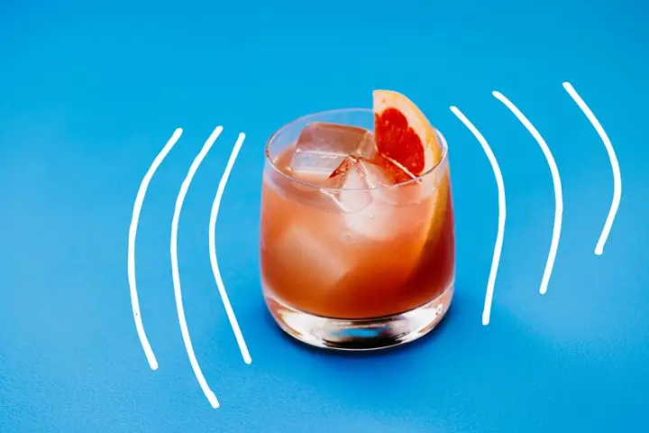 Photo illustration of pink Lounge Chair Afternoon cocktail in rocks glass with grapefruit garnish on blue background with white hand-drawn lines