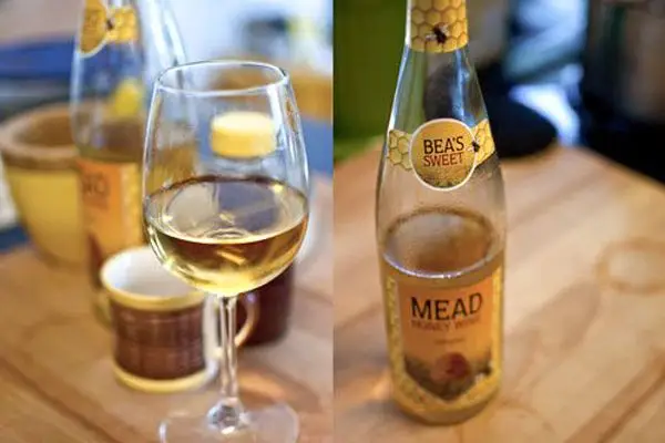 Two side-by-side photos: The one on the left shows a half-full glass of yellow mead on a wooden surface, a bottle behind it out of focus. The one on the right shows the same bottle facing forward, with a label that reads Bea