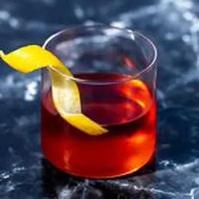 Sazerac, reddish brown, in rocks glass without ice, garnished with lemon twist, on a dark marble background