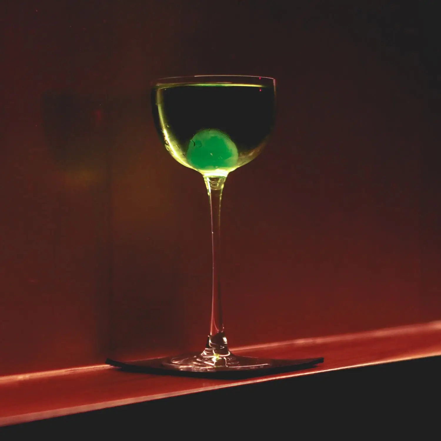 The Greenhorn cocktail, neon green and on black linen bar napkin, on bar in low light
