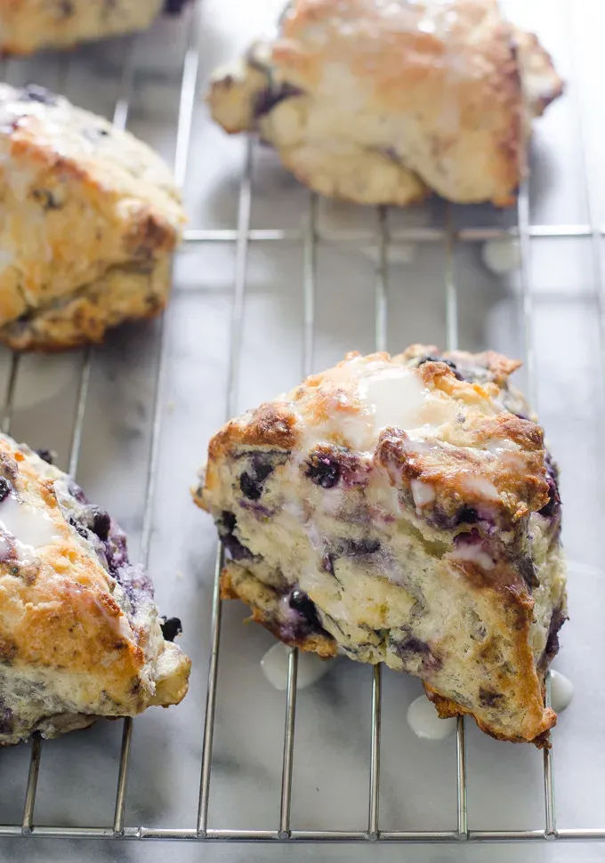 Blueberry Scones on a cooling rack drizzled with a Greek yogurt lemon glaze.' title='Easy Blueberry Greek Yogurt Scones Recipe with Lemon