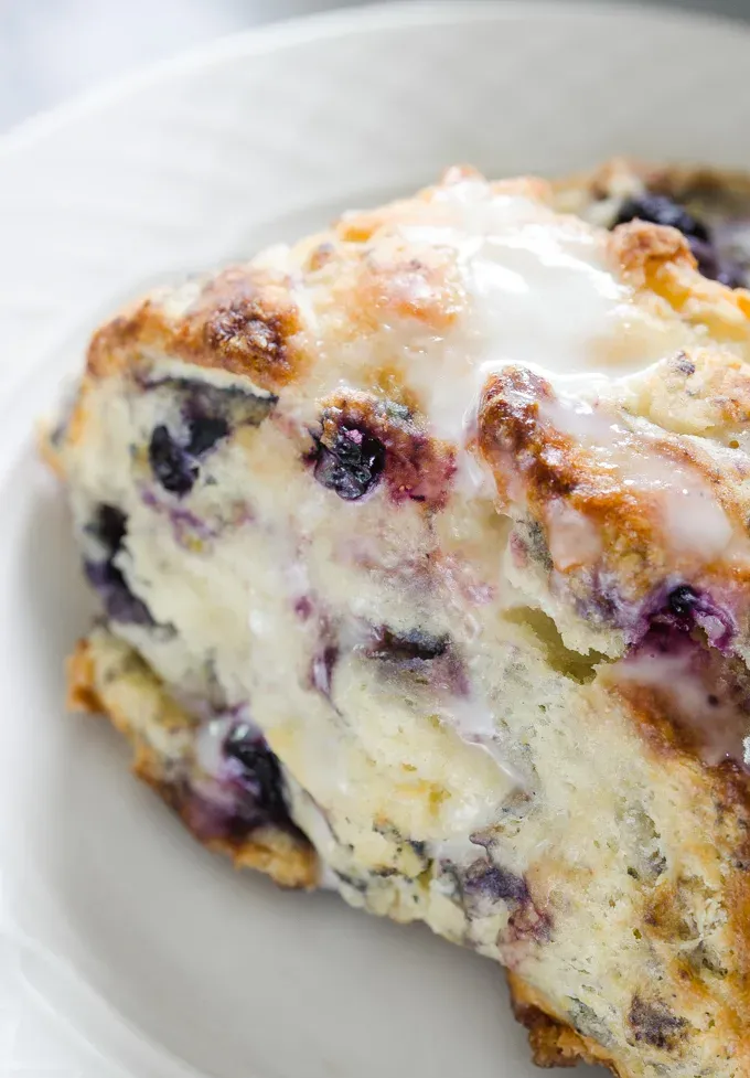 Close up shot of a blueberry scone drizzled with lemon-yogurt glaze.' title='Easy Blueberry Greek Yogurt Scones Recipe with Lemon