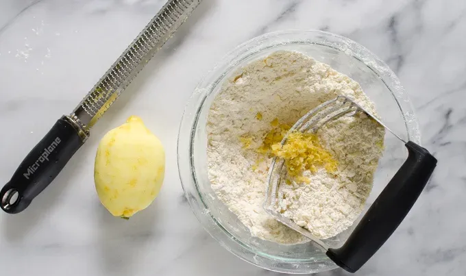 Cutting butter and lemon zest into the dry ingredients with a microplane zester off to the side.' title='Easy Blueberry Greek Yogurt Scones Recipe with Lemon
