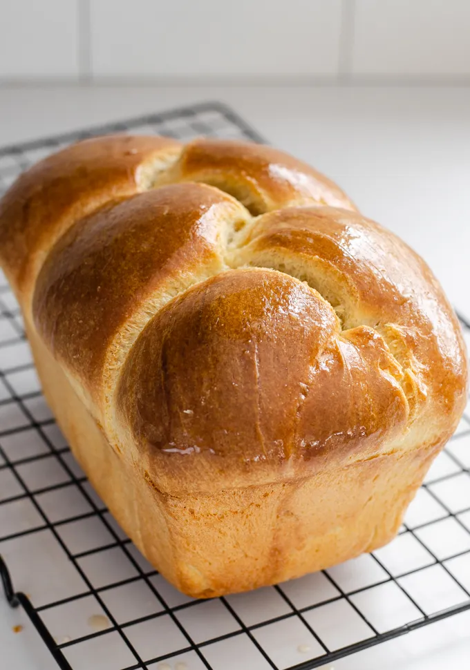 A loaf of sourdough brioche bread on a black wire cooling rack.' title='Sourdough Brioche