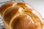 A loaf of sourdough brioche bread on a black wire cooling rack.' title='Sourdough Brioche