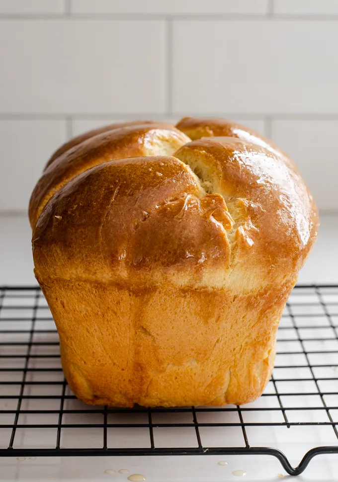 A loaf of sourdough brioche bread on a black wire cooling rack.' title='Sourdough Brioche