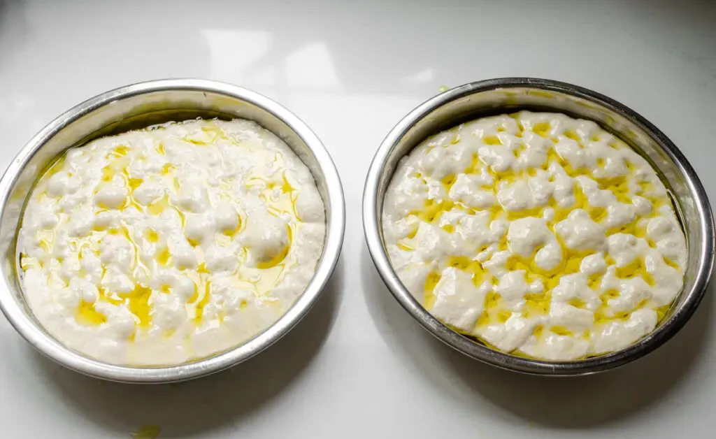 Two round cake pans of sourdough focaccia with olive oil drizzled on top.' title='Sourdough Focaccia Recipe