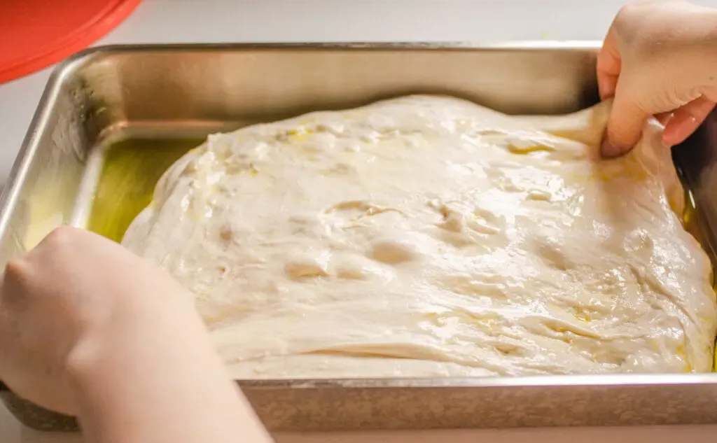 Stretching out the sourdough focaccia dough in the pan.' title='Sourdough Focaccia Recipe