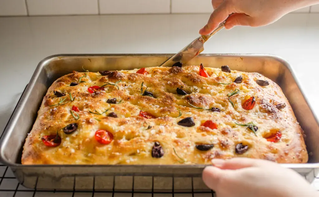 Running a knife around the edges of the cooked sourdough focaccia.' title='Sourdough Focaccia Recipe