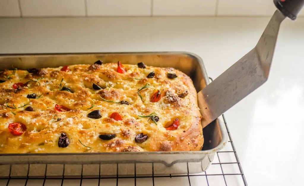 Using a metal spatula to remove the focaccia from the pan.' title='Sourdough Focaccia Recipe