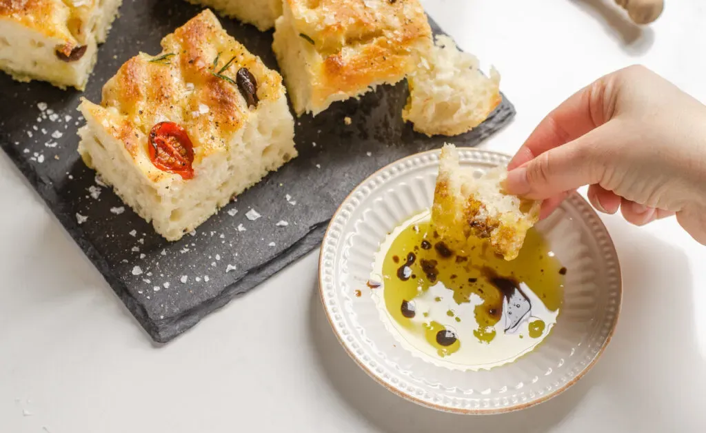 Dipping the sourdough focaccia into a little plate of extra virgin olive oil and balsamic vinegar.' title='Sourdough Focaccia Recipe