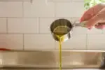 Pouring extra virgin olive oil into a pan to grease it in preparation for putting the focaccia dough in it.' title='Sourdough Focaccia Recipe