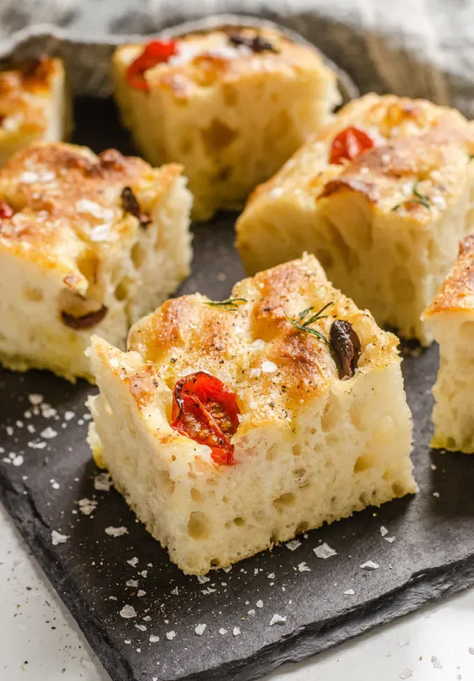Pieces of sourdough focaccia on a slate board with flaky sea salt and freshly ground pepper.' title='Sourdough Focaccia Recipe