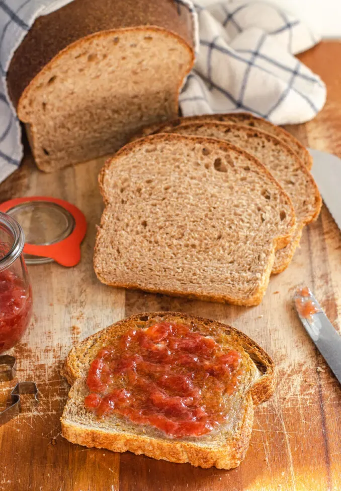 A toasted slice of whole wheat sourdough sandwich bread with butter and jam and more slices of bread in the background a jam jar to the left and a knife to the right.' title='Healthy Whole Wheat Sourdough Sandwich Bread