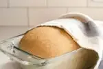 A risen loaf of healthy sourdough bread made with whole wheat flour with a tea towel partially on top.' title='Healthy Whole Wheat Sourdough Sandwich Bread