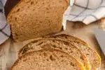 A loaf of healthy whole wheat sourdough sandwich bread on a cutting board with a few slices in the foreground with the loaf in the background with a tea towel on top.' title='Healthy Whole Wheat Sourdough Sandwich Bread