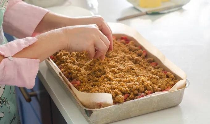 Adding the crumb mixture on top of the strawberry rhubarb filling and cake.' title='Strawberry Rhubarb Crumb Cake