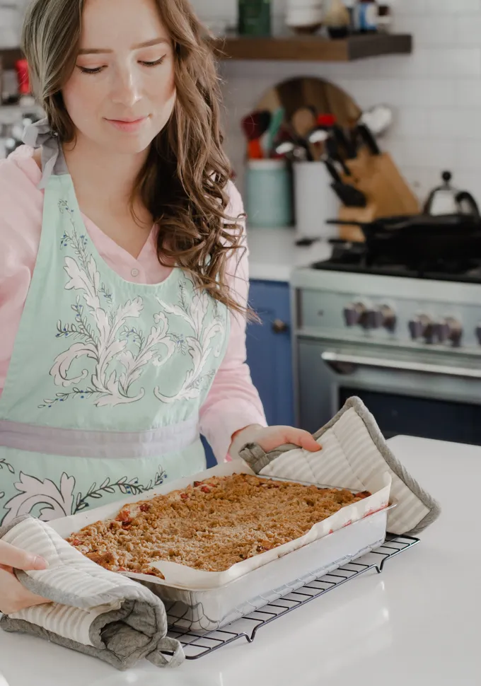Taking a pan of strawberry rhubarb crumb cake out of the oven and placing it on a wire cooling rack.' title='Strawberry Rhubarb Crumb Cake