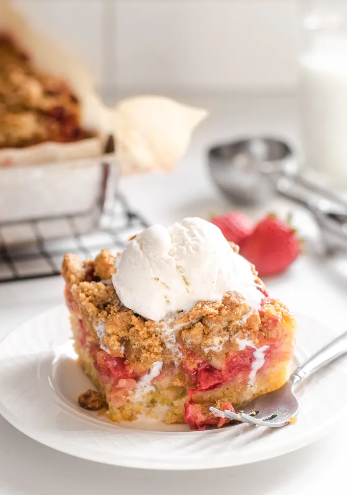 A slice of strawberry rhubarb cake with a scoop of melting vanilla ice cream on top.' title='Strawberry Rhubarb Crumb Cake