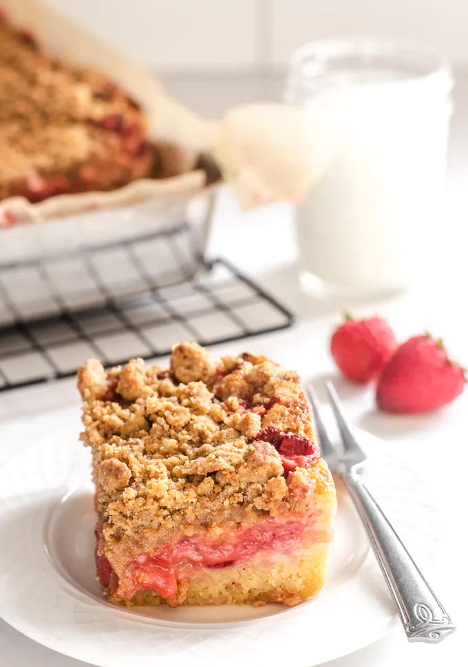 A slice of strawberry rhubarb cake with the cake pan in the background and a small dessert fork on the plate.' title='Strawberry Rhubarb Crumb Cake