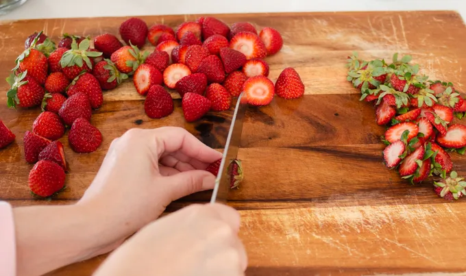 Chopping strawberries on a wooden cutting board.' title='Strawberry Rhubarb Crumb Cake