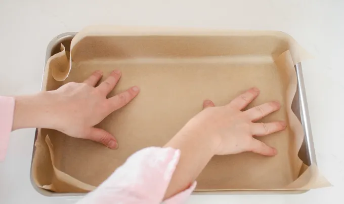 Lining a 13x9-inch baking pan with parchment paper.' title='Strawberry Rhubarb Crumb Cake