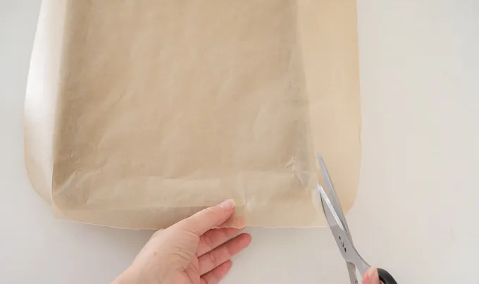 Cutting slits into a piece of parchment paper to make it fit into a baking pan neatly.' title='Strawberry Rhubarb Crumb Cake