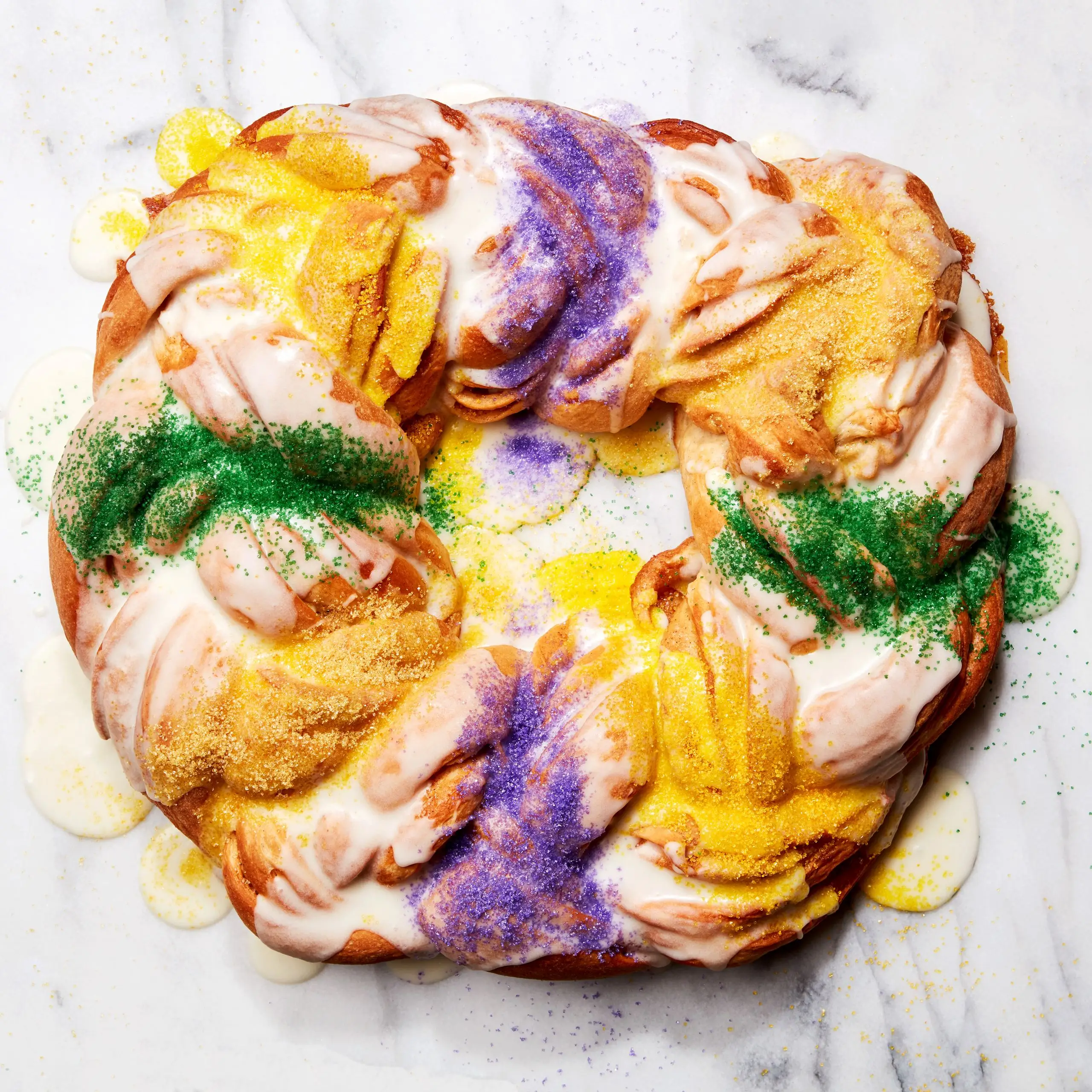 A king cake with icing and colored sugar on a marble surface.
