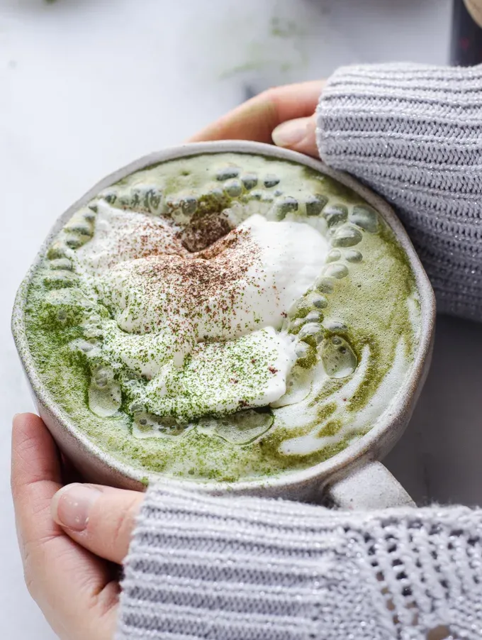 Hands around a mug of matcha cocoa AKA matcha hot chocolate.' title='Matcha Cocoa