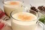 Two mugs of homemade eggnog with a tea towel greenery and fresh nutmeg around them.' title='Homemade Eggnog
