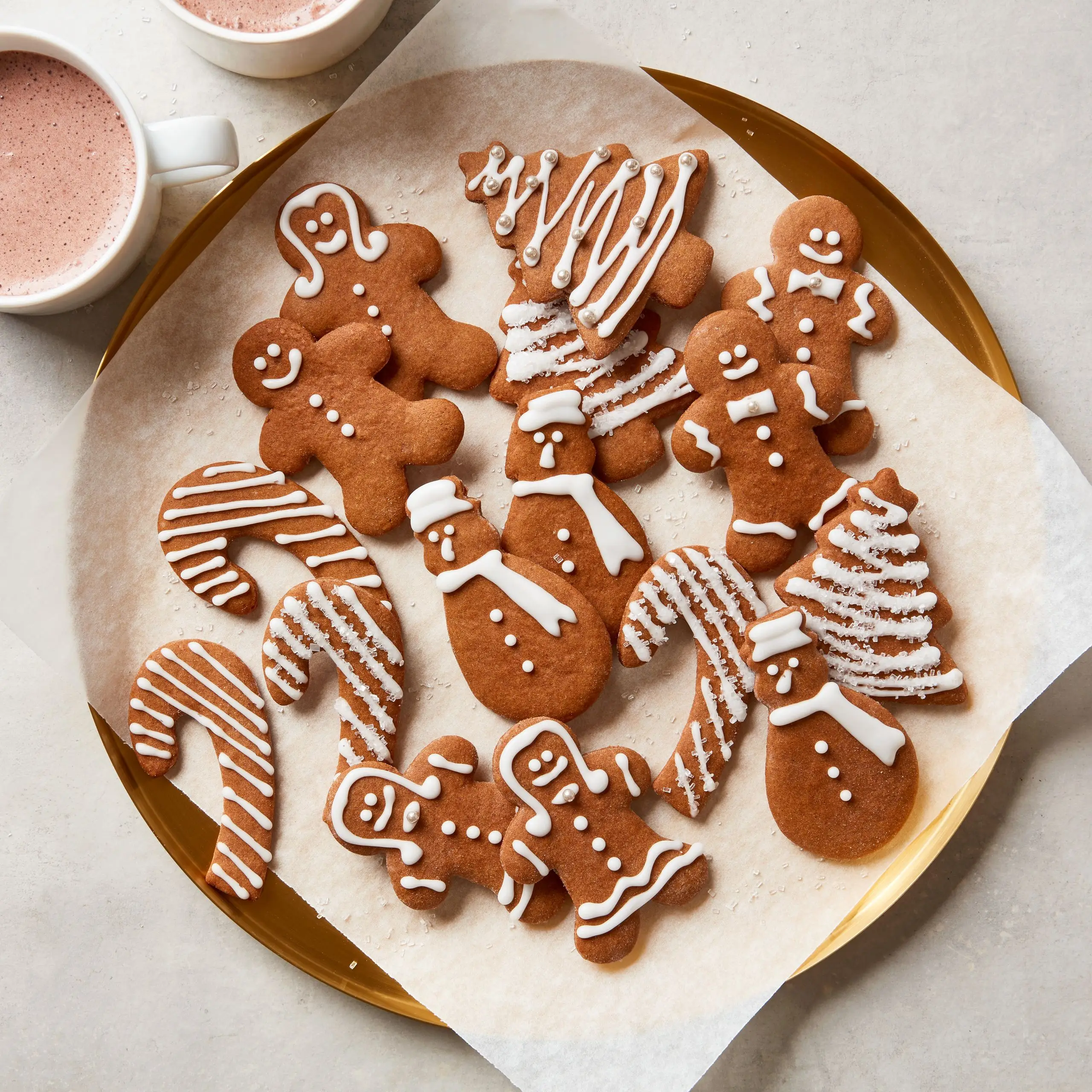 A platter with gingerbread Christmas cookies in assorted shapes including gingerbread men snowmen candy canes and trees.