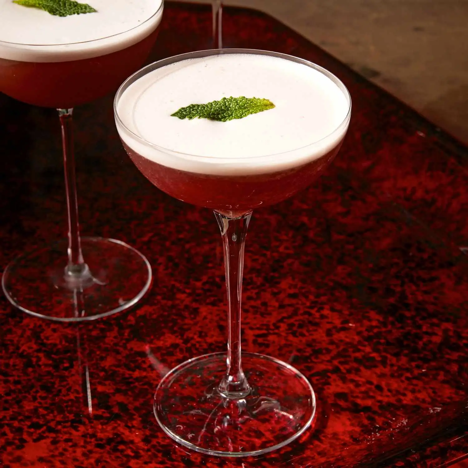Clover Leaf cocktail in stemmed coupe glass on red tray, with single mint leaf garnish floating in foam