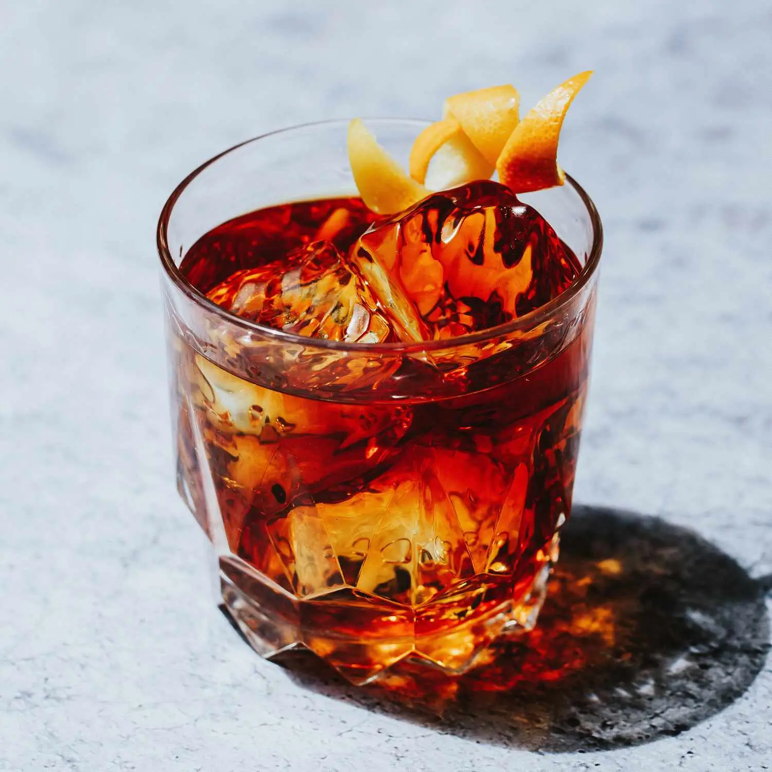 Tender Nob stirred brown cocktail with two ice cubes and orange twist in rocks glass, set on marble surface 