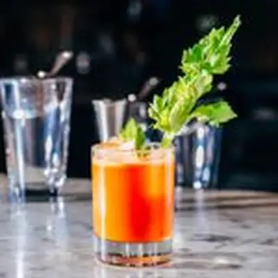 bright-orange Lunar Eclipse cocktail in a rocks glass, garnished with a leafy celery stick and served on a bar in front of glasses and tools
