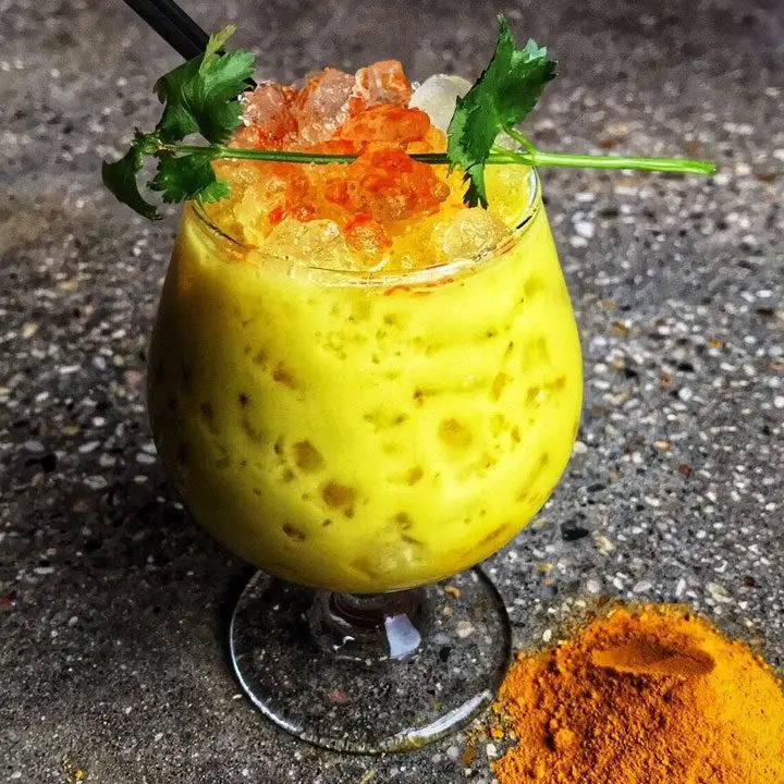 bright-yellow anti-inflammatory cocktail in a snifter, garnished with chili oil and a cilantro sprig