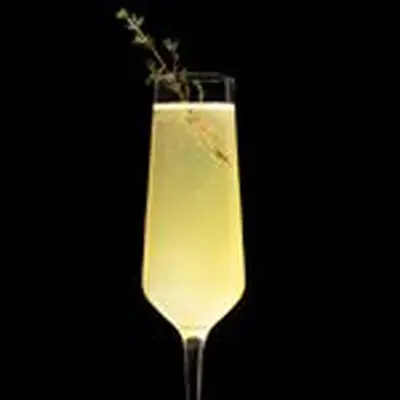 A narrow Champagne flute holds a bubbly yellow drink garnished with a sprig of thyme. It glows brightly against a black background