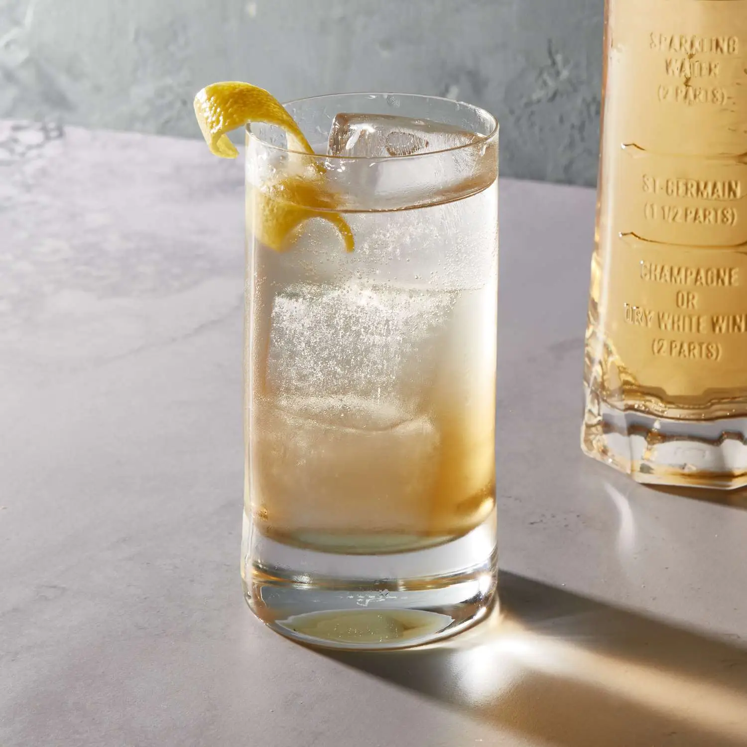 St-Germain cocktail in highball glass, with St-Germain measuring glass in the background holding extra spritz
