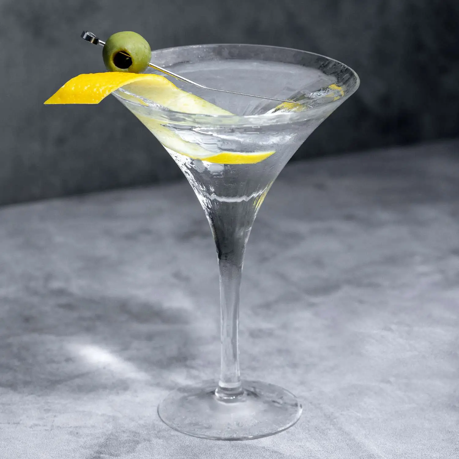Vodka Martini in a classic V-shaped Martini class with both lemon twist and olive garnish, on dark marble background