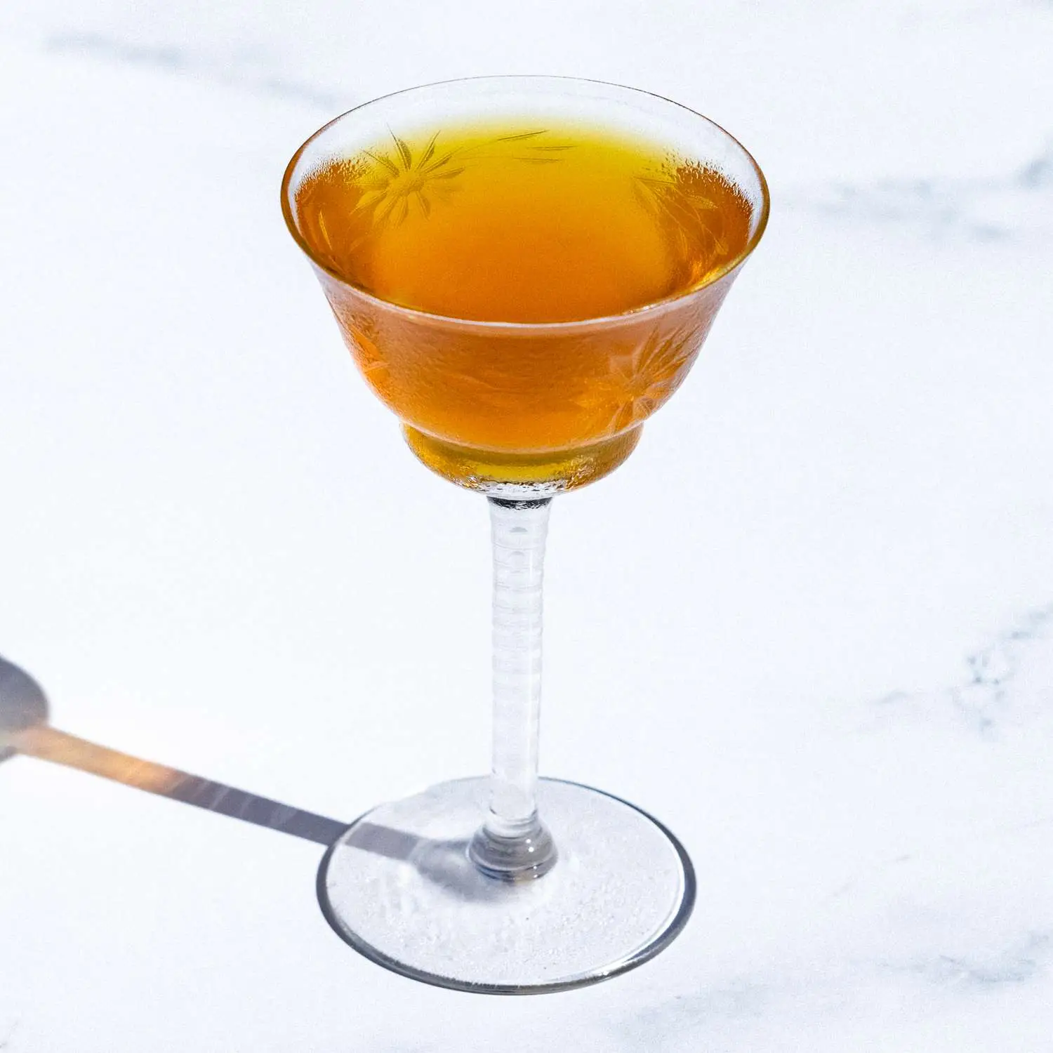 Bushwick cocktail, pale brown, in stemmed coupe glass with flower etchings