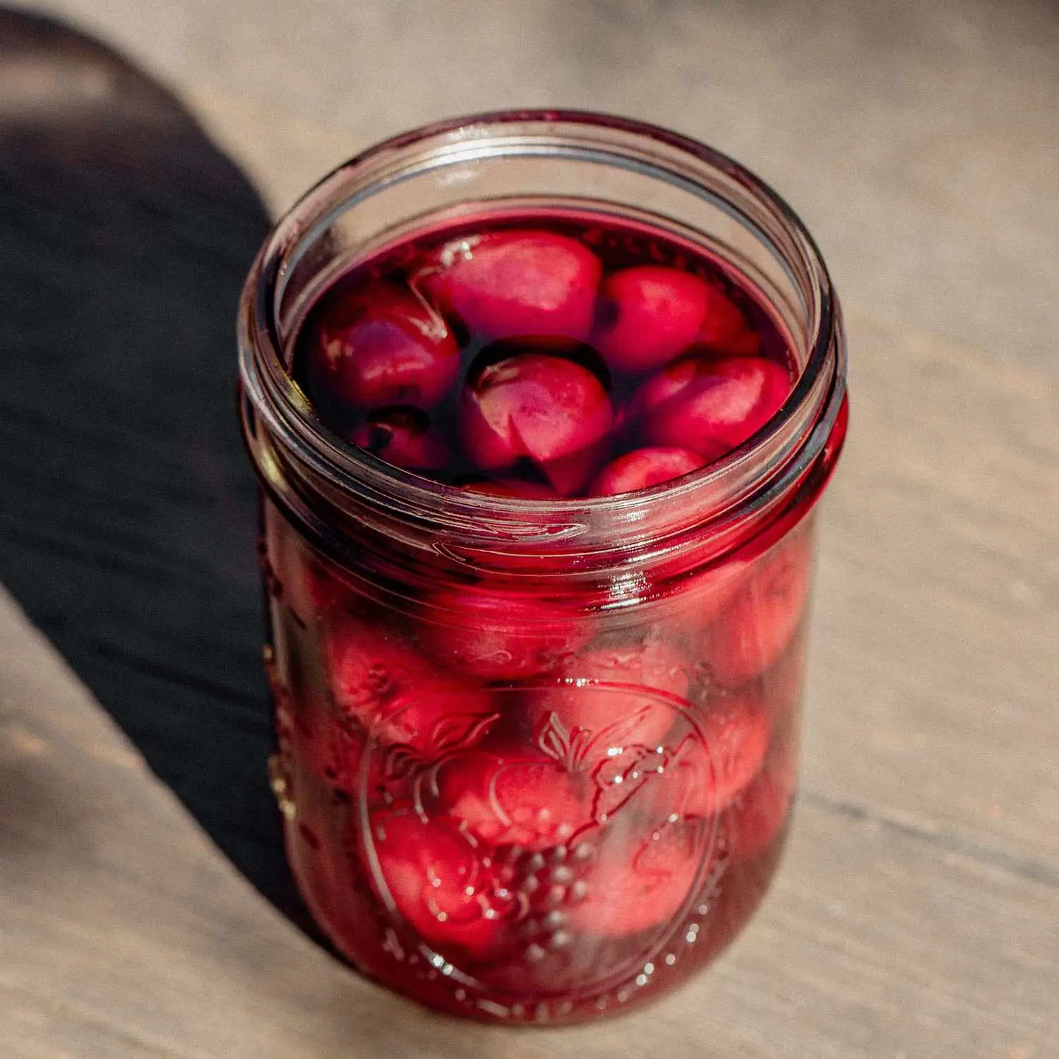 Homemade brandied cocktail cherries in open mason jar on wood table