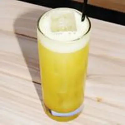 yellow-colored Delhi Cooler cocktail in a Collins glass, served over ice with a black straw