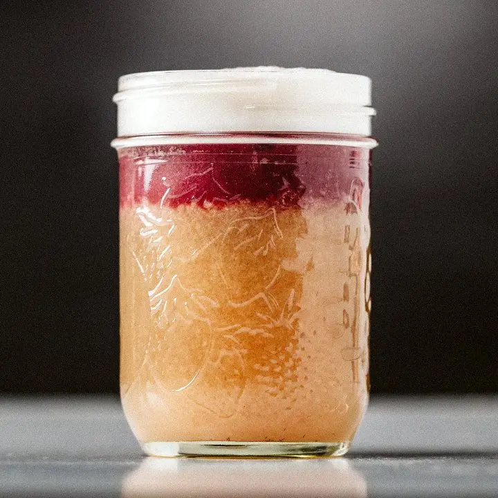 A small Mason jar holds a dark orange drink with a band of red wine and a float of egg whites on top.
