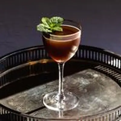 Death by Morning cocktail in gold-rimmed Nick & Nora class with mint sprig garnish, on metal serving tray