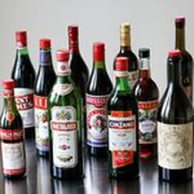A group of 11 sweet vermouth bottles on a steel surface